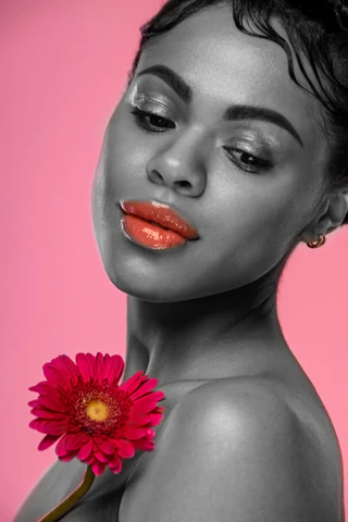 A black woman holding a flower on a pink background.