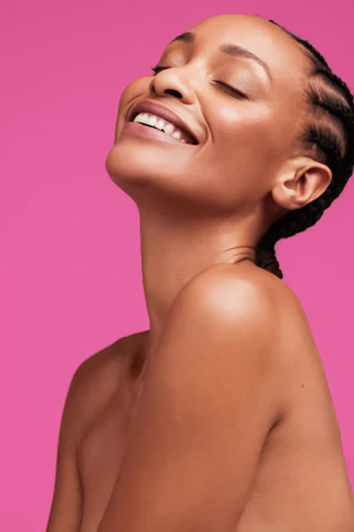 A black woman smiling on a pink background.